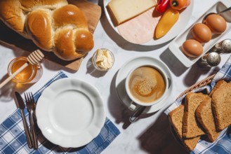 Breakfast with toast, stollen, honey, cheese, ham, coffee, butter, peppers and eggs on a table