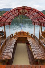 Interior view of a wooden boat with a red and white roof floating on a calm lake, Lake Bled, Lake