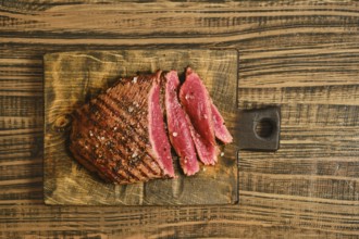 Beef is sliced into thick pieces and placed on a wooden cutting board. The meat shows a reddish