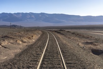 Curving railroad tracks lead through the arid landscape of La Puna, Argentina, with distant
