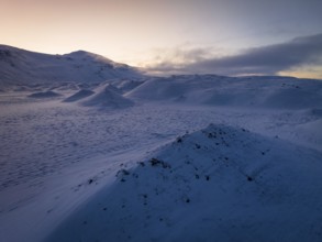 A serene winter twilight spreads over snow-draped hills in Iceland, capturing the tranquil beauty