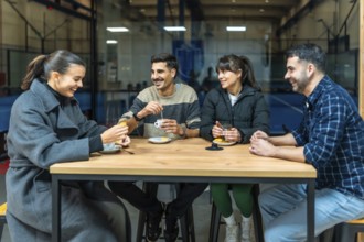 Four diverse friends are sitting at a wooden table, drinking coffee and talking, relaxing together