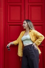 A fashionable woman in a vibrant yellow shirt stands confidently against a bright red door on a