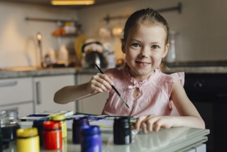 A joyful child with a painted nose engages in a creative painting activity at home. She holds a