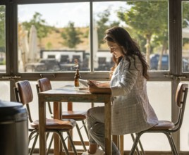 A woman sits in a sunny cafe, engaged with her tablet. Sunlight pours through the window, creating