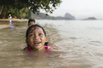 Two children enjoy swimming in the warm, shallow waters of a beach in the Philippines, surrounded