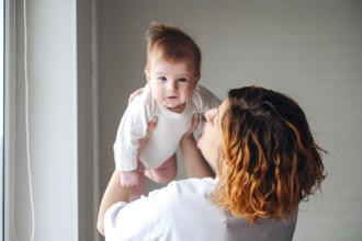 A mother lovingly holds her smiling newborn baby girl near a sunlit window, capturing a moment of