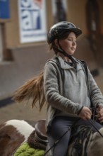 Little girl, 10 years old, in the saddle on a horse in an indoor riding arena,