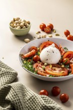 A vibrant salad featuring creamy burrata, juicy tomatoes, and crunchy pistachios. Served in a white