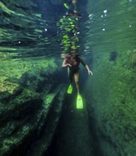 Underwater view of a woman with flippers snorkeling in the crystal clear waters of a natural pool