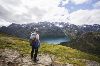 Adventurer stands on a rocky ridge, overlooking a serene turquoise lake surrounded by Norway's