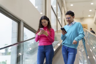 Young man and woman, Gen Z friends, enjoy using their smartphones while riding an escalator in a