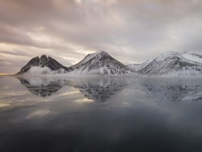 Captivating view of Iceland's Stokksnes mountains reflecting on the calm, icy waters. Snow-dusted