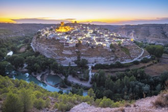 A breathtaking view of the historic town of Jorquera, Spain, perched on a cliff at sunset. The