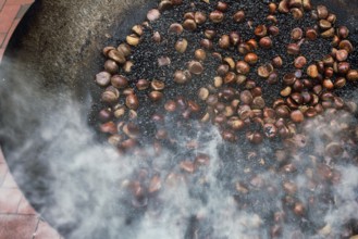A traditional cooking scene from Hong Kong showing chestnuts being roasted in a large metal wok,