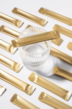 From above an esthetic arrangement of golden jelly collagen sachets with a clear glass resting on a