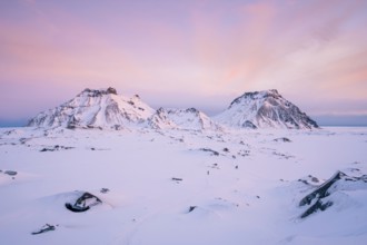 A breathtaking view of Katla Glacier's rugged snow-covered mountains beneath a pastel pink sunrise