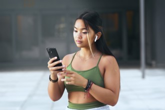 A young Chinese woman wearing a green top and wristbands, holding a smartphone and listening to