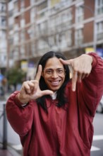 A joyful man in a red jacket creates a frame with their hands, emphasizing focus and perspective.