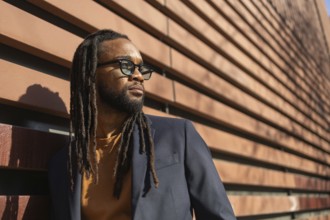 A cuban business man with sunglasses leans against a modern wall in sunlight, showcasing a blend of