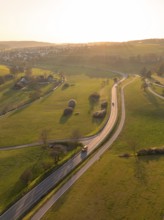 Winding country road through green fields and trees, under a warm sunset sky, Gechingen, district