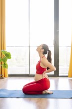 A pregnant woman practices yoga in a serene setting, embracing wellness and relaxation. She kneels
