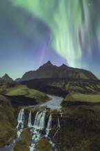 Breathtaking view of the Aurora Borealis cascading over a serene Icelandic waterfall surrounded by