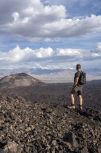 Hiker looks at a vast volcanic landscape under a cloudy sky, Argentina, volcanoes, lava field,