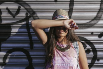A stylish woman in a hat with chic accessories poses in front of a graffiti-covered metal door,