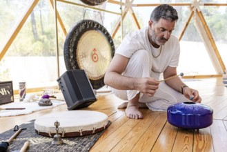 A male sound therapist conducts a sound therapy session with steel tongue drum, and other