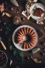 A delicious chestnut cake sits elegantly on a rustic table, surrounded by autumn leaves and pine