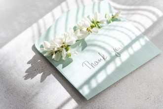 Top view of delicate spring snowdrops arranged on a pastel thank you card, with natural sunlight