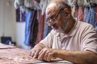 A senior Iranian master skillfully restores a traditional carpet in his well-equipped workshop in
