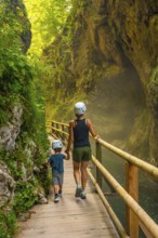 Mother and son wearing helmets are walking on a wooden walkway, exploring the beautiful vintgar