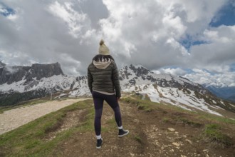 A woman stands at Passo Giau in the Dolomites, Italy, gazing at the snow-covered mountains under