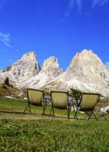Three camping chairs in a meadow at Passo Sella in front of dramatic mountain peaks under a clear