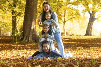 Asian family having fun in an autumn park, with laughter and playful energy. Children enjoying time