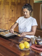 A woman in a white shirt bakes fresh cookies in a cozy kitchen. She places them on a cooling rack