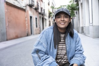 Latina woman wearing a striped shirt and denim jacket smiles confidently while sitting on a vibrant