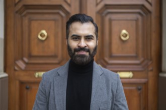 Portrait of a confident Indian businessman in a grey coat and black turtleneck, standing in front