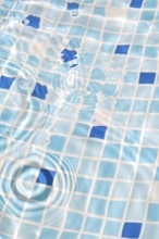 A close-up image of mosaic tiles under clear, rippling water, creating a serene and refreshing