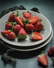 A collection of ripe, red strawberries on a ceramic plate, some halved to show their juicy interior