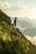 A man takes a break from trail running to hydrate, standing on a scenic mountain path with distant