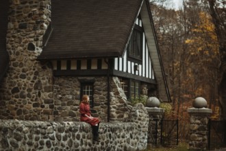 A woman sits by a rustic stone cottage in the Quebec countryside, surrounded by the warm colors of