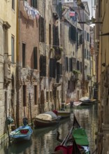 Narrow canal between tall old buildings, lined with boats in a quiet, historic neighbourhood,
