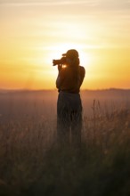Young woman taking pictures at sunset, standing in tall grass, Lake Victoria, Uganda