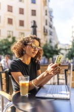 Vertical photo of a young Moroccan female freelancer working with mobile and laptop in a sidewalk