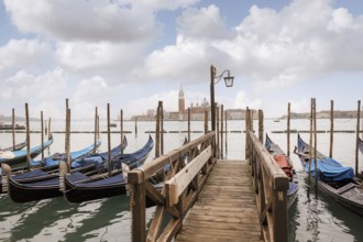 Scenic view of a wooden dock leading to gondolas in Venice, Italy. The background showcases the
