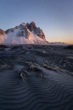 A stunning view of Stokksnes Mountain in Iceland, illuminated by the warm light of sunrise. The