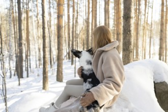 Unrecognizable woman holding a border collie in a snowy forest, sharing a peaceful moment